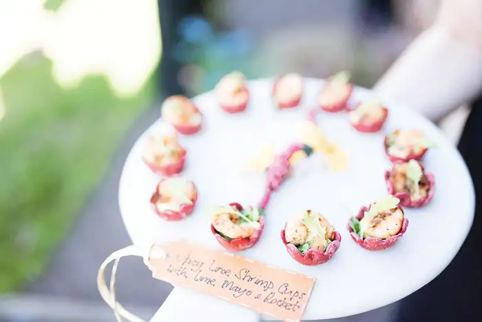 Waiter holds platter of entrees with note saying "Spicy lime shrimp cups with lime mayo & rocket"