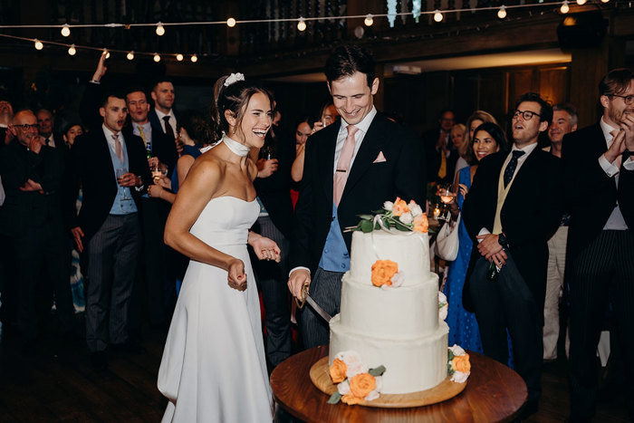 a bride and groom cutting a wedding cake surrounded by wedding guests.