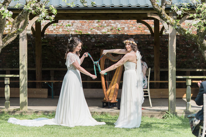 two brides knotting tartan fabric during outdoor wedding ceremony at Byre at Inchyra