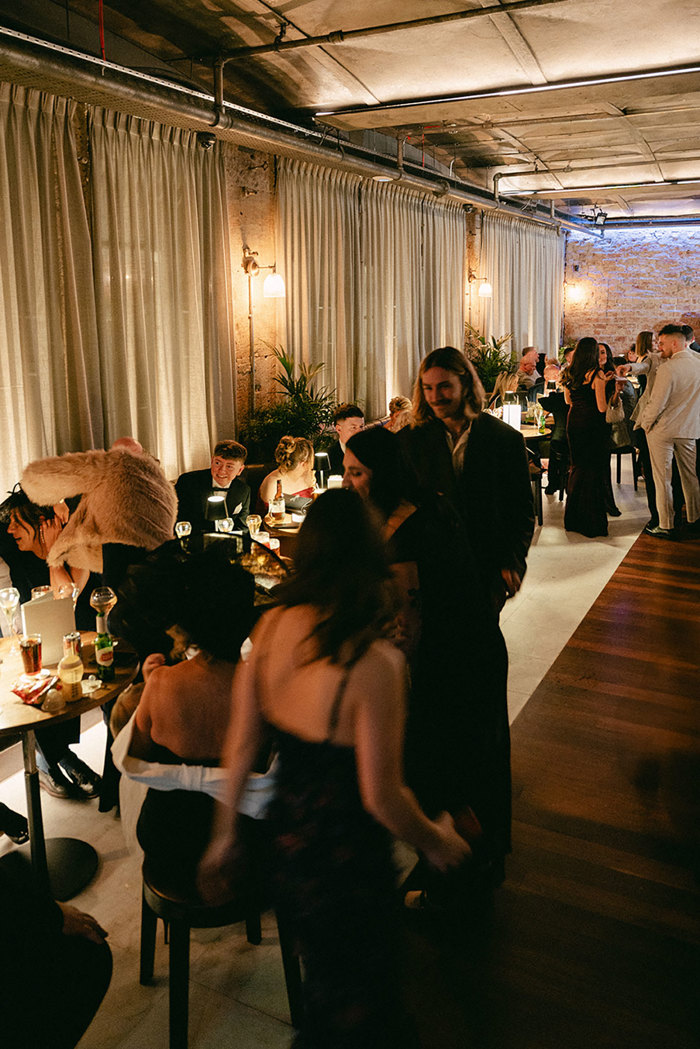 a dimly lit room with curtains all along one side and different groups of formally dressed men and women chatting and having a drink