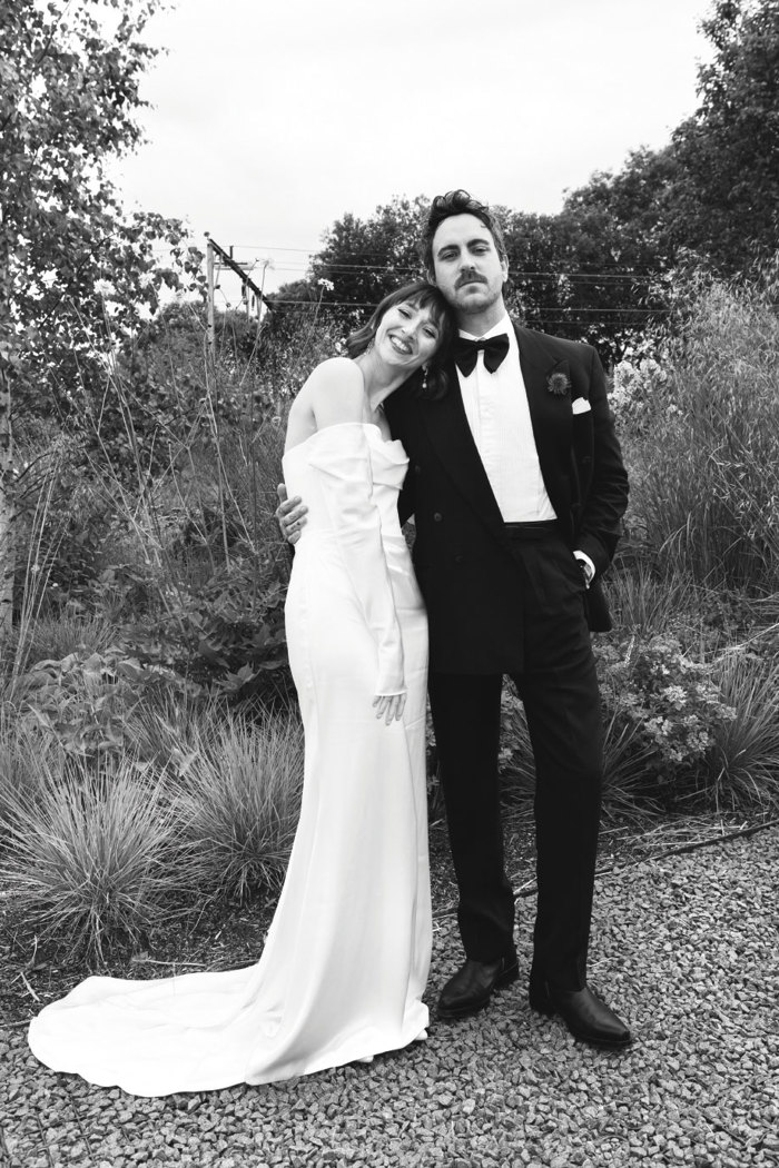 a bride laying her head on a groom's shoulder in a garden setting 