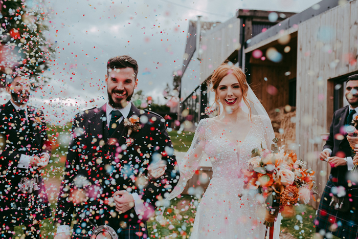 Guests throw confetti at couple as they walk through the crowd