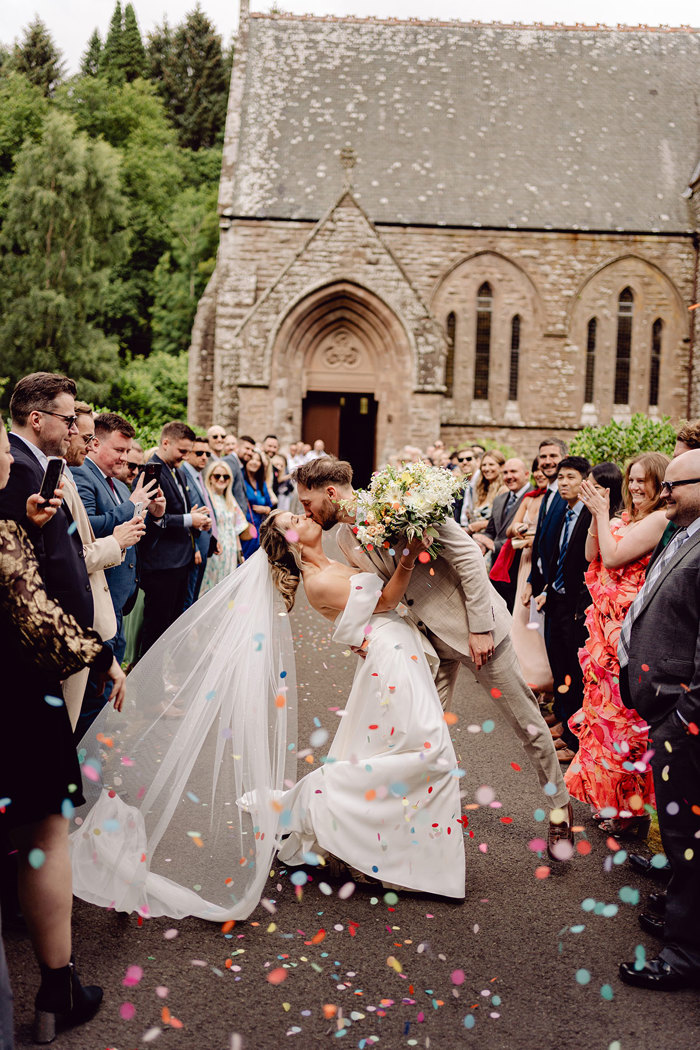 guests throw confetti over bride and groom as they kiss after wedding ceremony at drumtochty castle