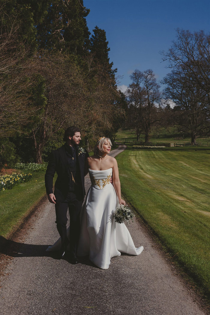 A bride and groom walking along a path in a garden.