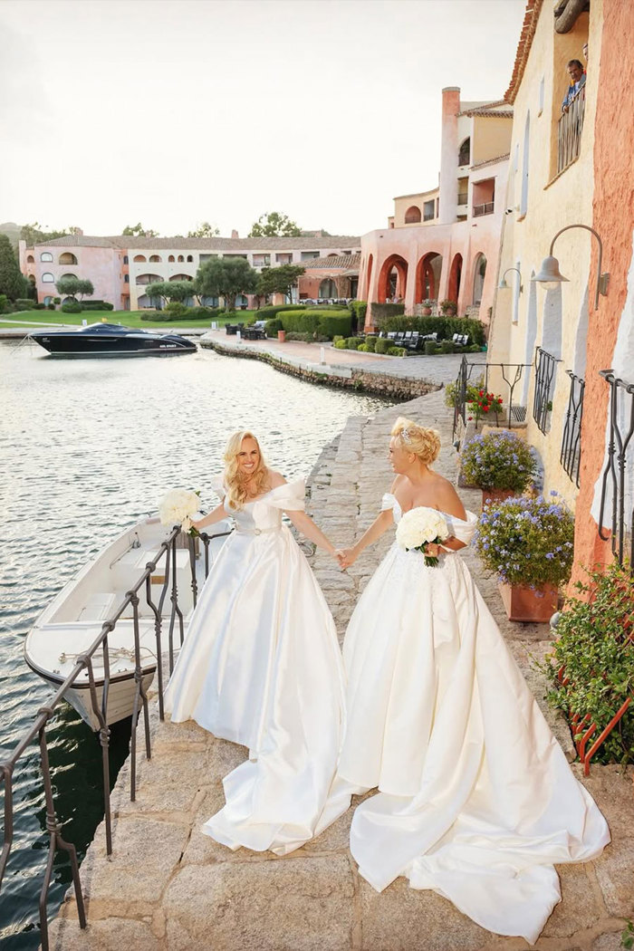 Rebel Wilson and Ramona Agruma on their wedding day wearing wedding dresses and standing by water