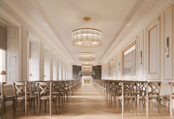 A long room with white walls, chandeliers and wooden chairs set out for a wedding ceremony