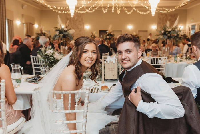 Bride and groom smile at top table with guests in the background