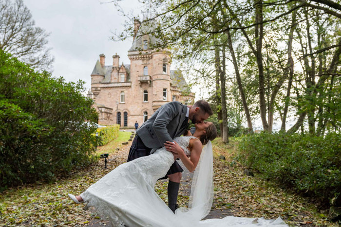 bride and groom dip kissing on leaf filled path outside the front of castle