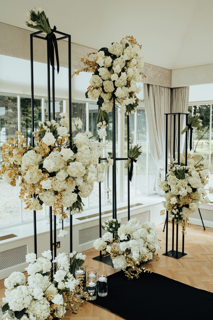 A floral display with white flowers on black stands with candles in glass jars