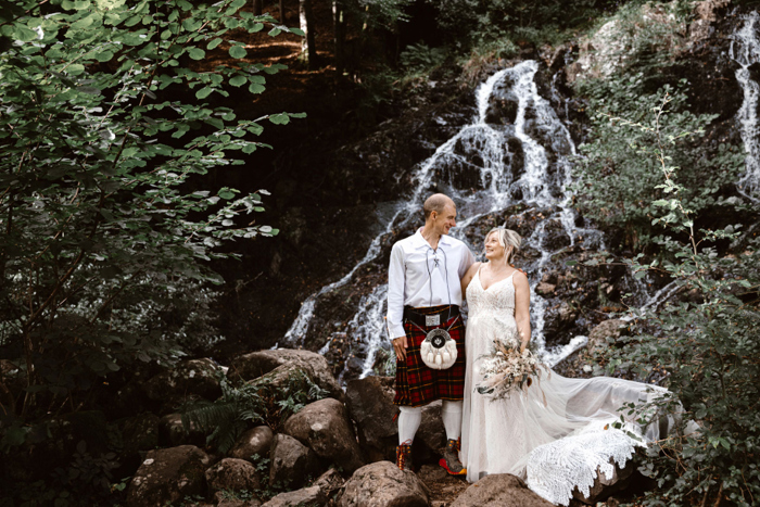 Bride and groom pose in front of a waterfall