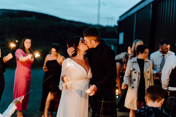 Bride and groom kiss holding sparklers