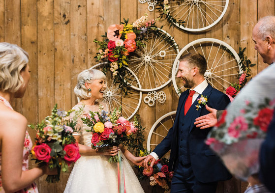 bride and groom get married with colourful flowers and bicycle wheels behind them