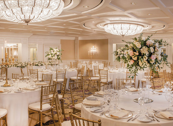 A large room filled with round tables and wooden chairs set up for a wedding meal