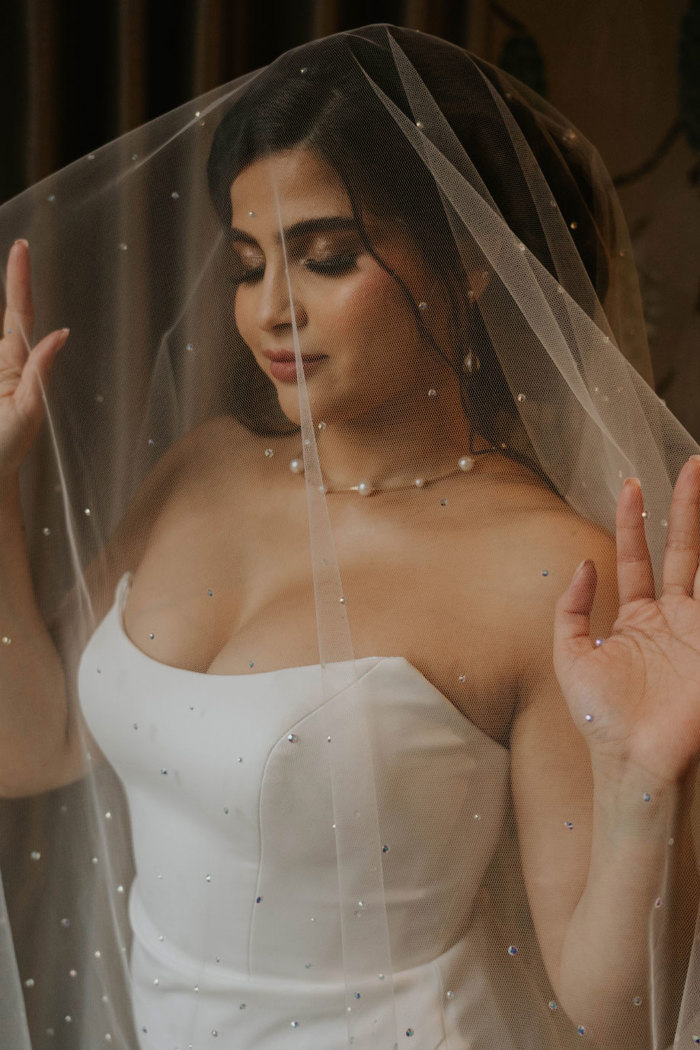 A bride underneath her veil which is covered in little pearls 