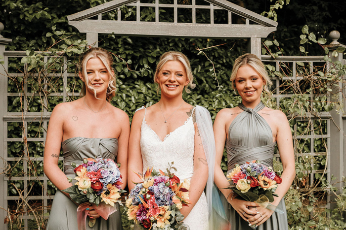 Bride and two bridesmaids smile holding colourful flowers