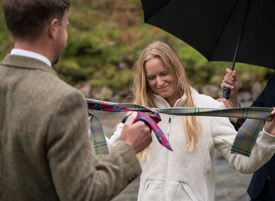 a bride and groom doing a handfasting with tartan ribbons under an umbrella