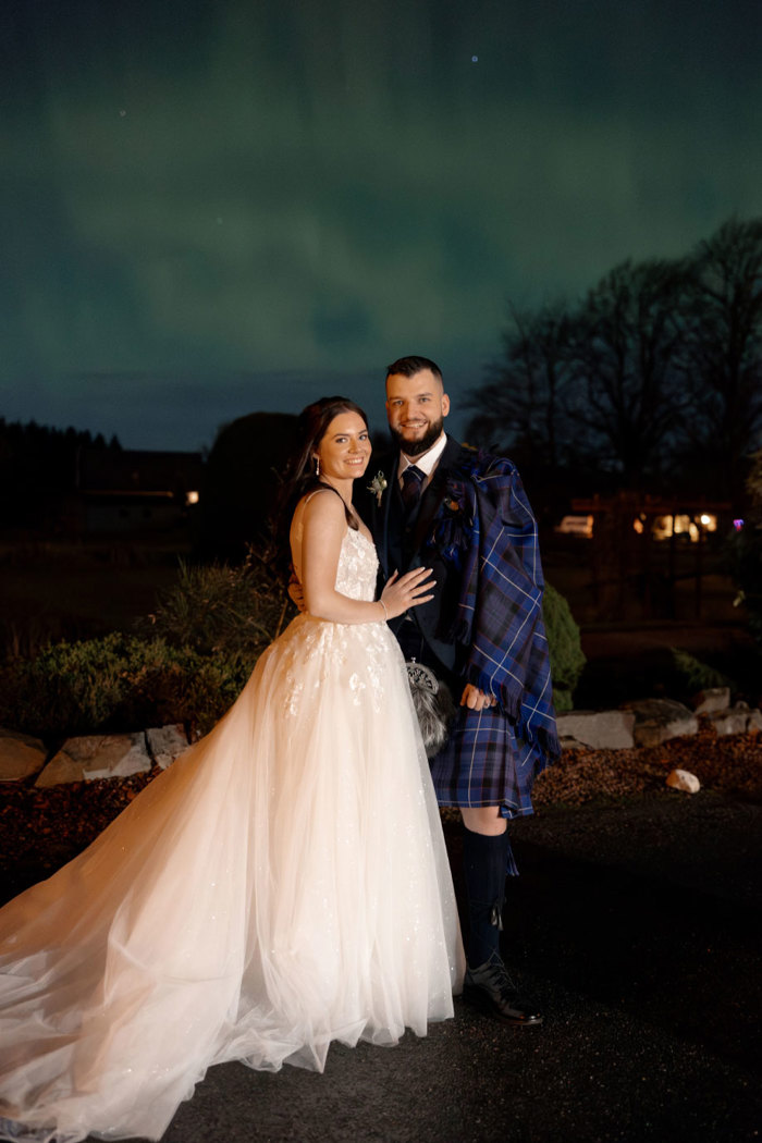 a bride and groom posing as the northern lights light up the sky