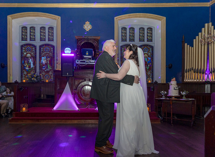 a bride and groom dancing in a church setting with stained glass windows behind them