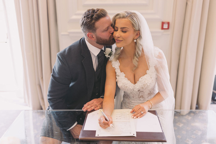 Groom kisses bride while they sign documentation