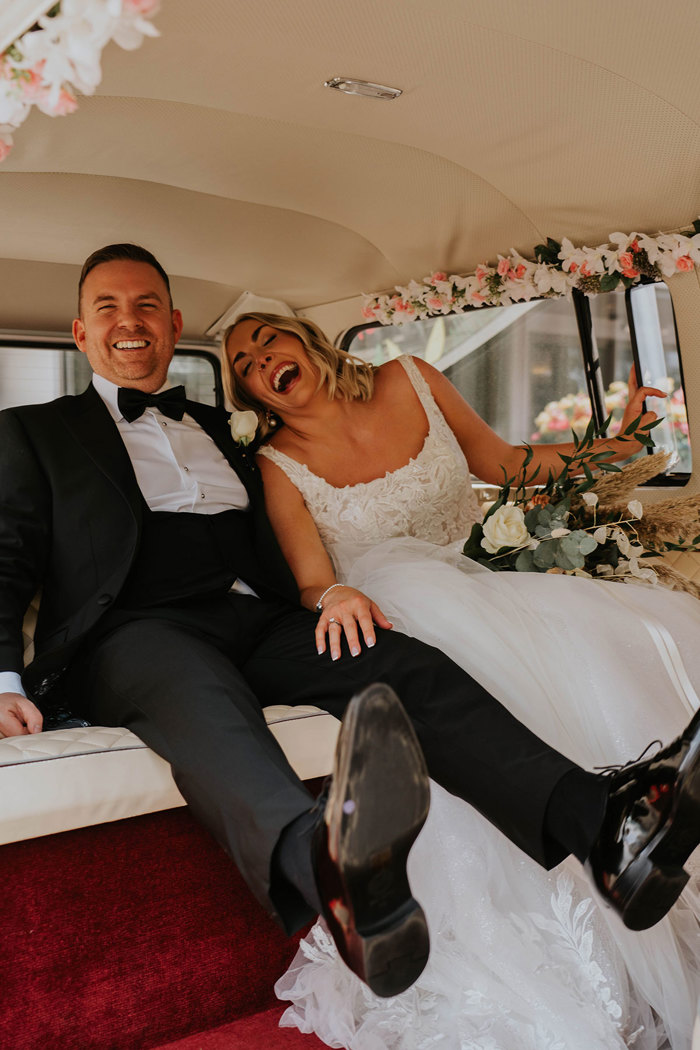 a laughing bride and groom sitting in a VW camper van.