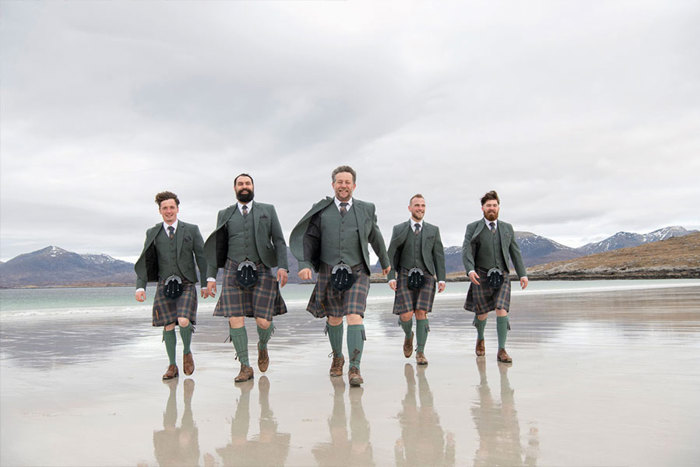 A group of men in kilts walking across a beach 