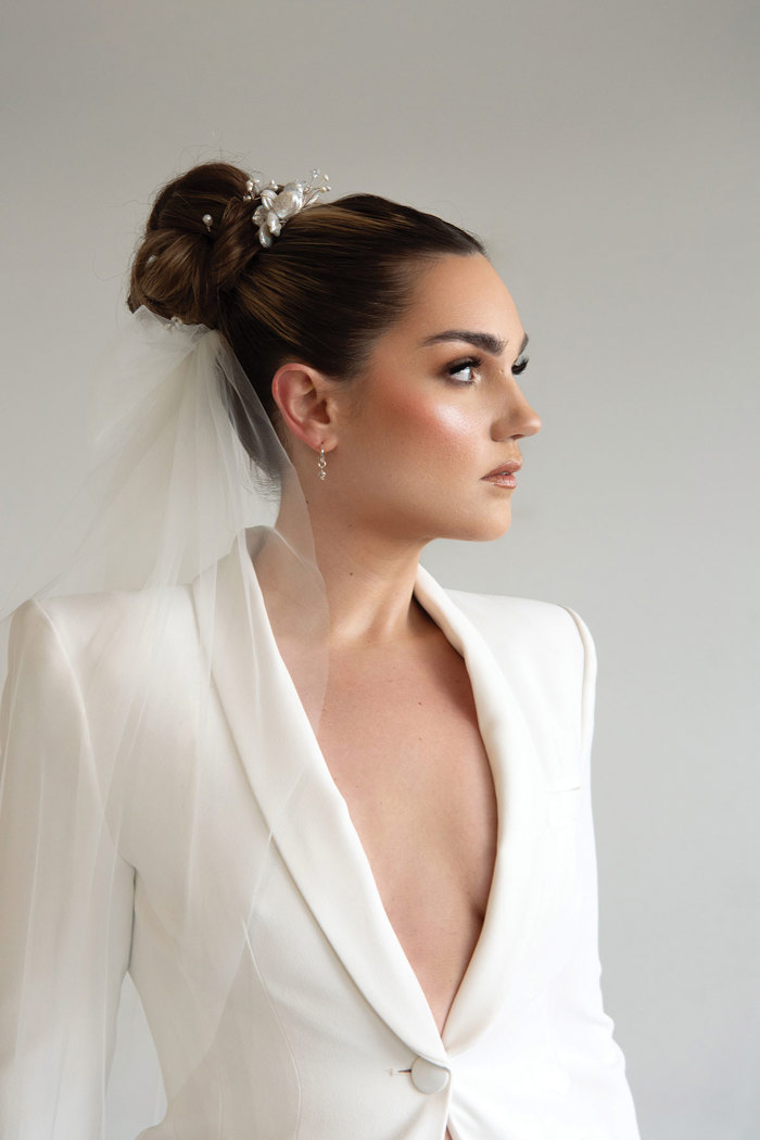 brunette model has her hair in high bun with veil and wears a low-cut white suit jacket