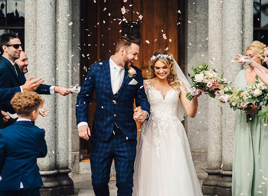 Bride and groom, now husband and wife, walk out of ceremony with flower petals thrown at them