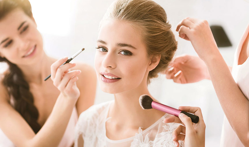 Hands with makeup brushes applying makeup and doing a person's hair 