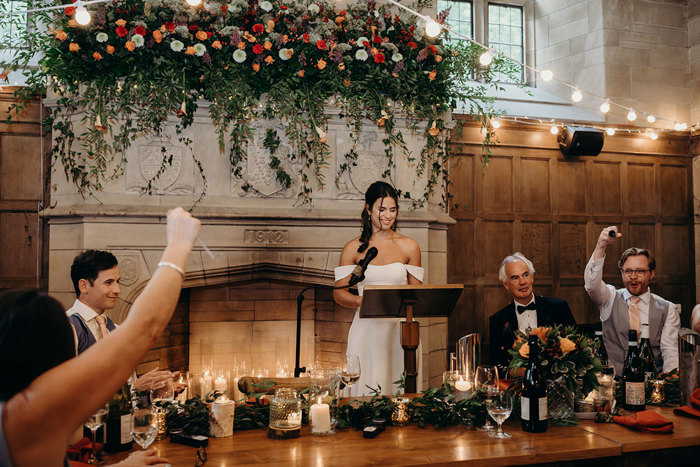 A person standing at a podium with a microphone in front of a person in a tuxedo. A large stone fireplace at Achnagairn Castle