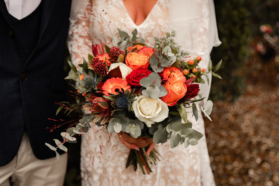 bride holds flower bouquet with orange tones and green foliage