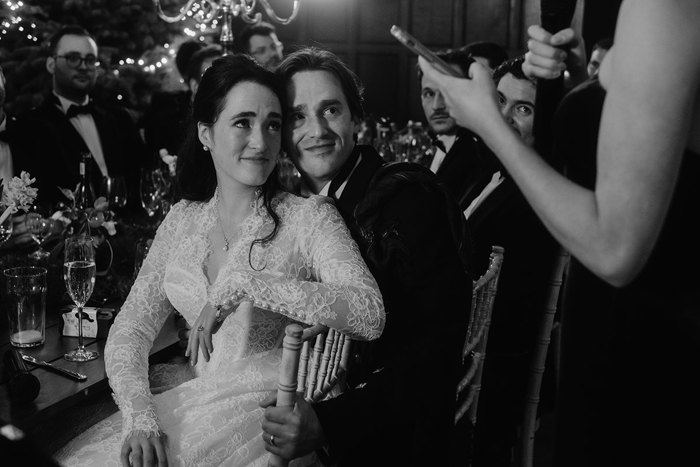 a seated bride and groom look at someone making a speech in front of them.