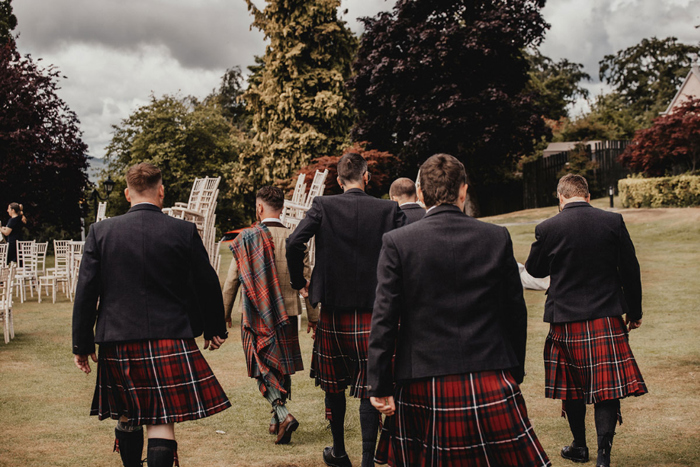 Groomsmen in kilts walk towards ceremony