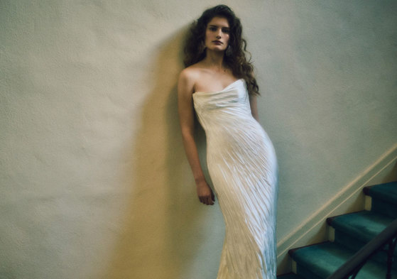 a model wearing a crinkled silk strapless wedding gown standing on stairs leaning against a wall