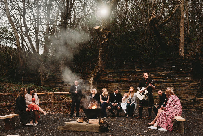 Guests gather round fire as someone plays guitar