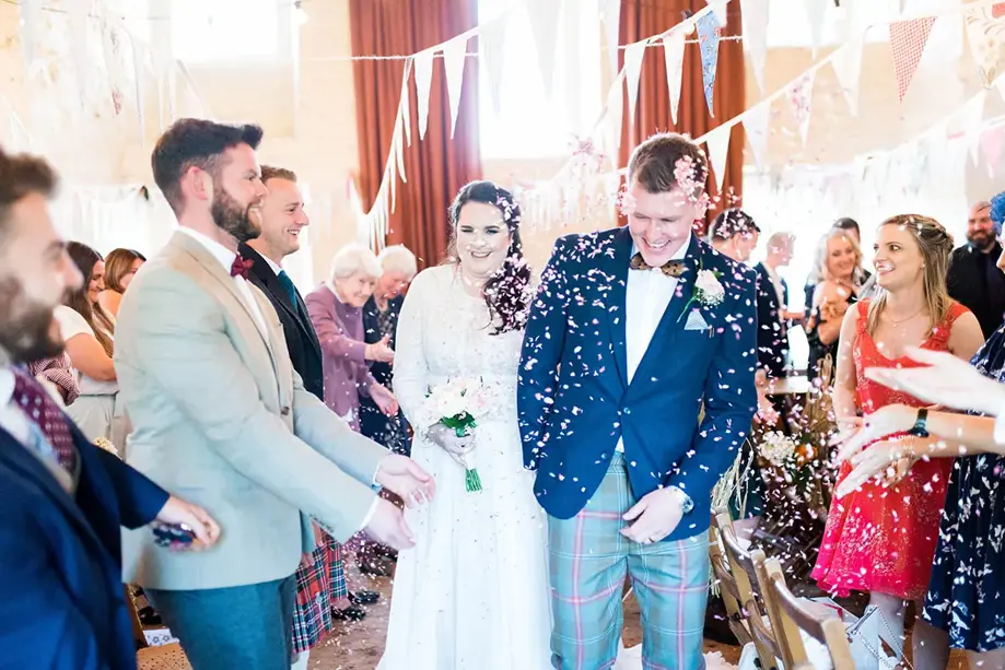 Bride and groom walk through confetti following their ceremony