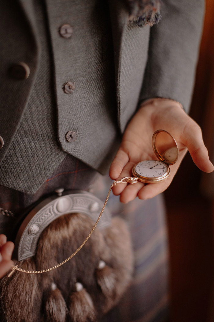 detail image of man in full green tonal kilt outfit with brown sporran who holds gold chained pocket watch in open palm