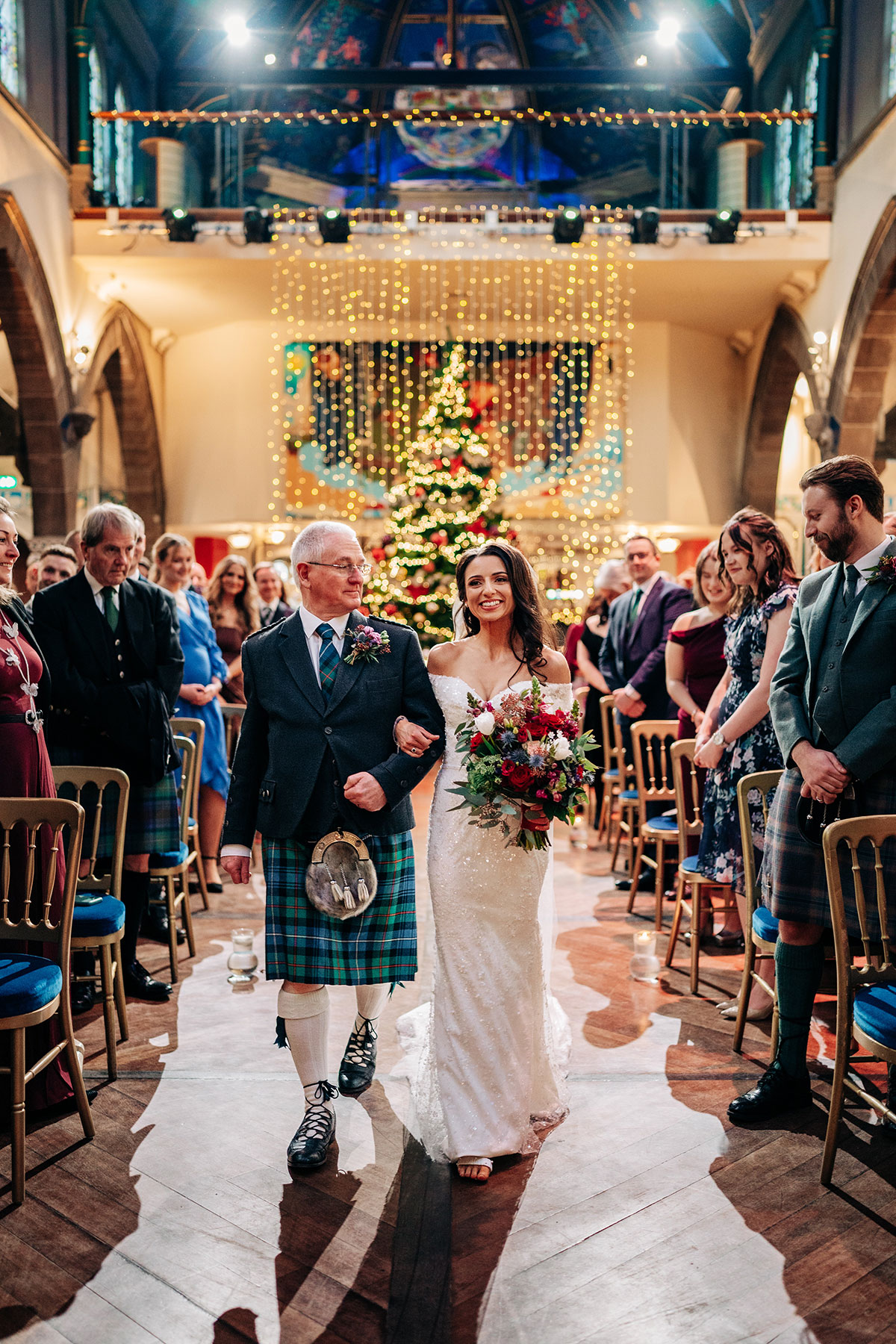 bride links arms with dad as she walks down the aisle at oran mor in glasgow