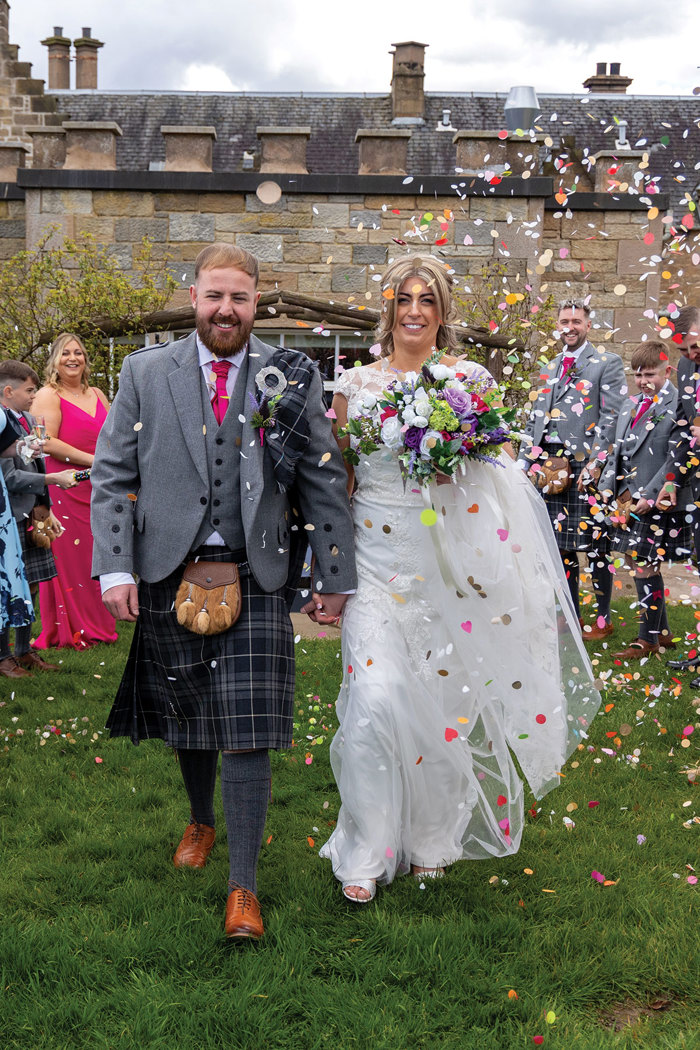 bride and groom smile as guests throw colourful confetti at wedding