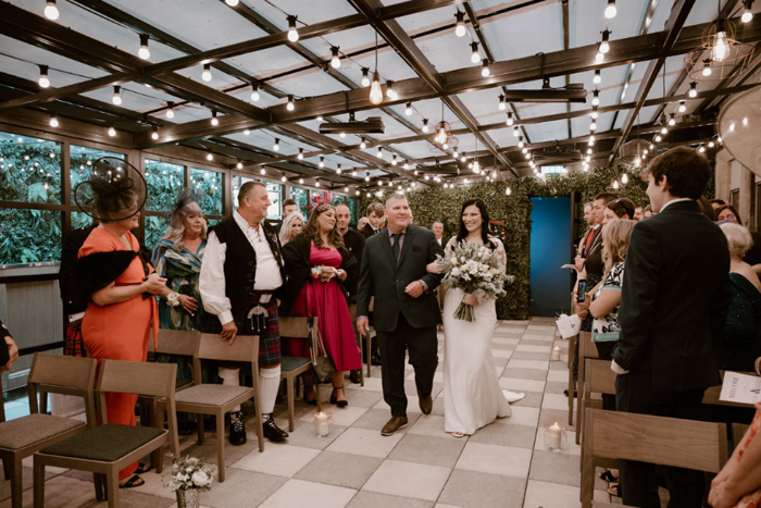 Bride is walked down the aisle by her dad carrying a bouquet 