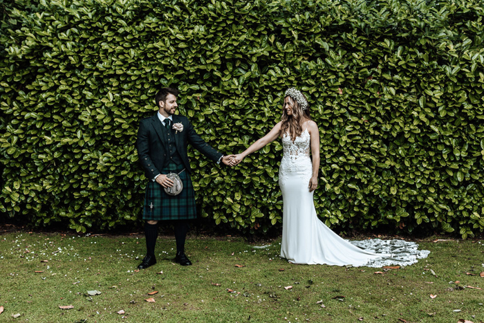 Couple hold hands in front of hedge