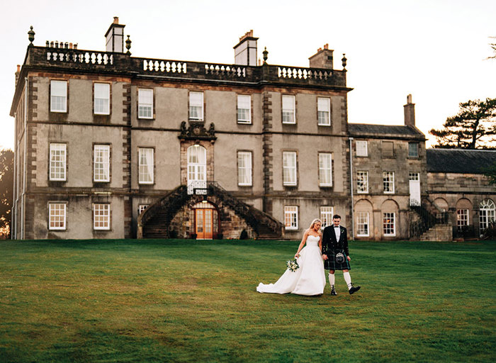 a bride and groom walking across a green lawn outside Dalmahoy Hotel and Country Club