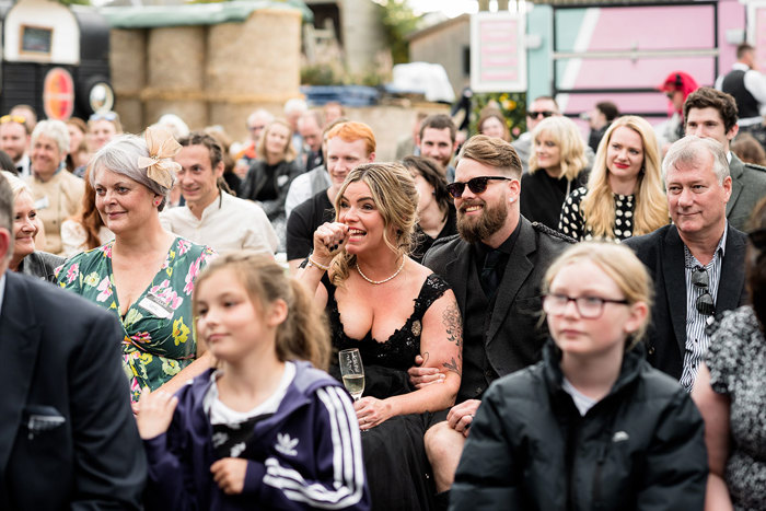 Shed Wedding A Bride And Groom Both Wearing Black Look On Nervously Smiling Surrounded By Wedding Guests