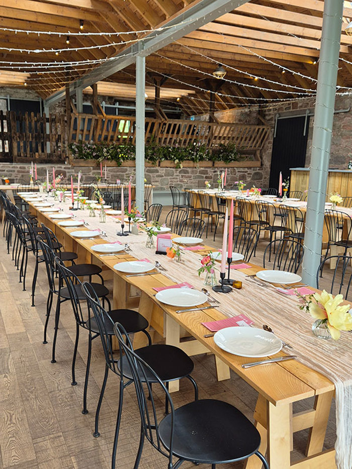 a long wooden table with a table runner, tall pink candlesticks and bud vases down the centre