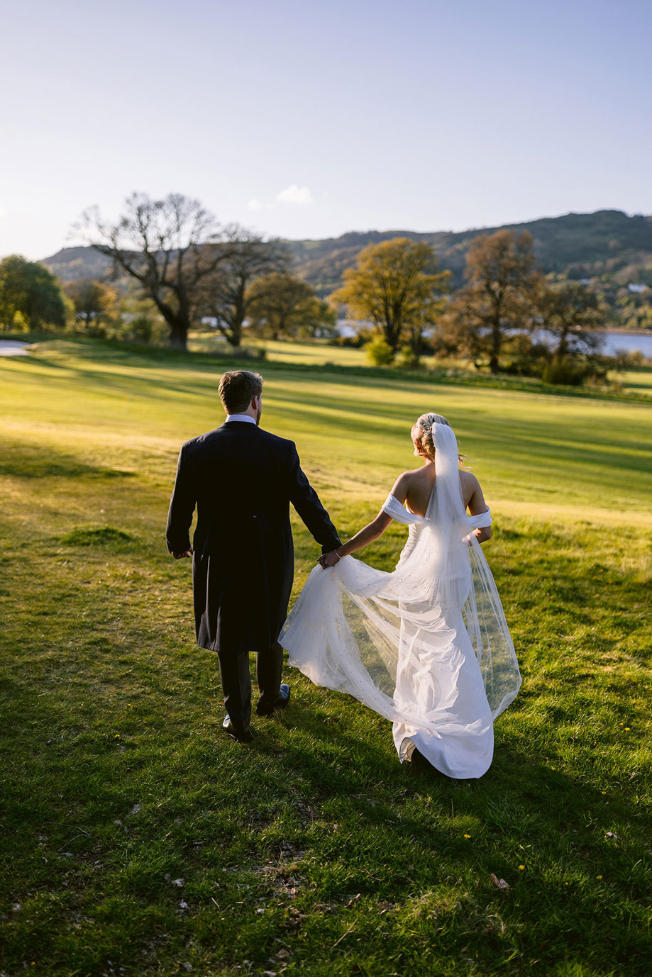 A bride and groom holding hands and walking on grass.