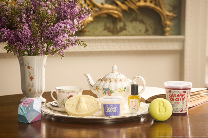 A selection of Lush bath and body products on a tray with a teapot next to a bouquet of purple flowers 