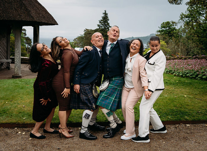 two grooms and four wedding guests pose in a garden setting