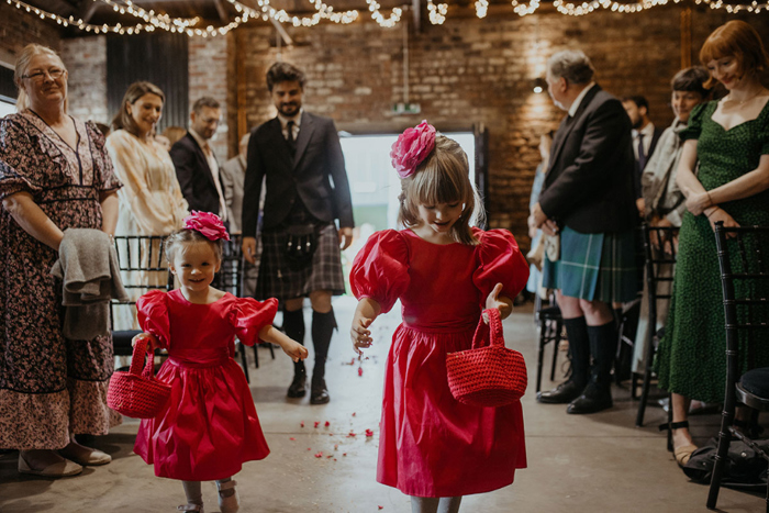 Flower girls wearing dark pink dresses spread petals on the aisle