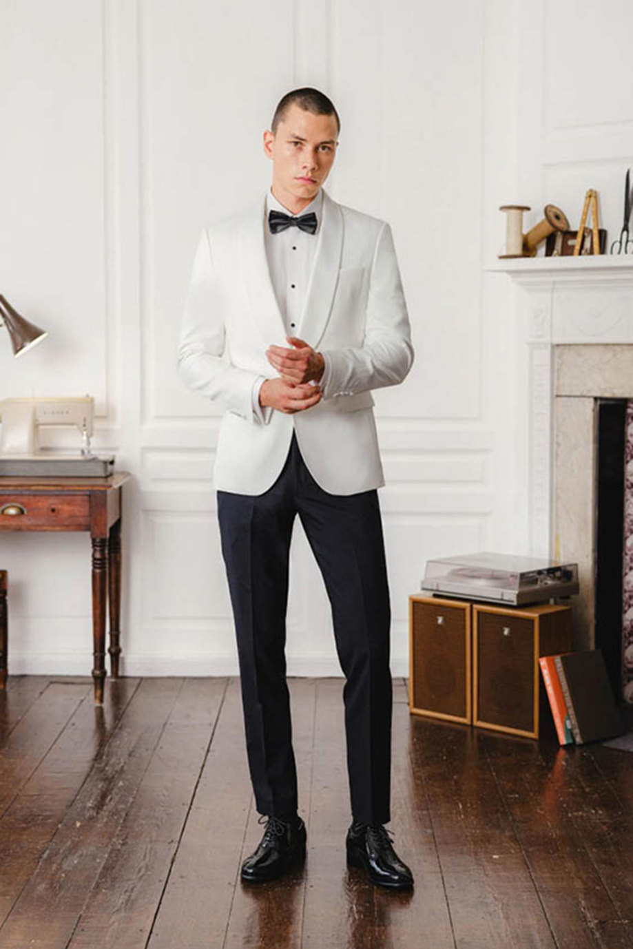 a model wearing a white suit jacket, bow tie and black trousers