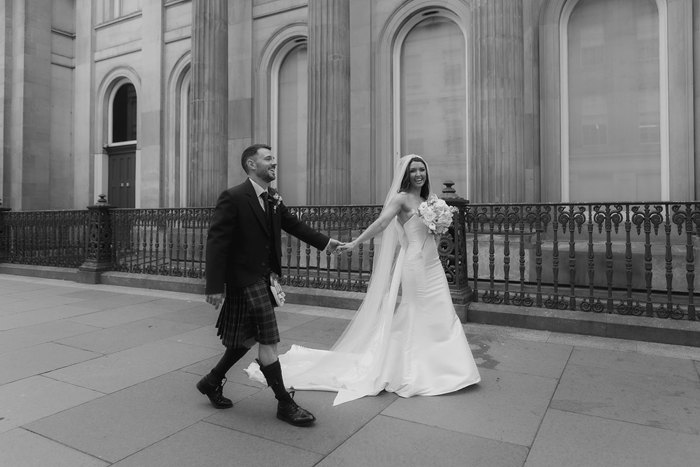 A black and white photo of a bride and groom holding hands and walking through Glasgow city centre