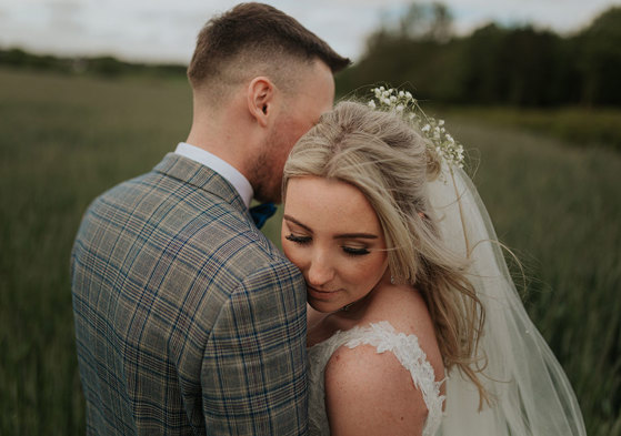  A close up of faces of a Bride And Groom Posing For A Wedding Photo In A Field Of Tall Grass